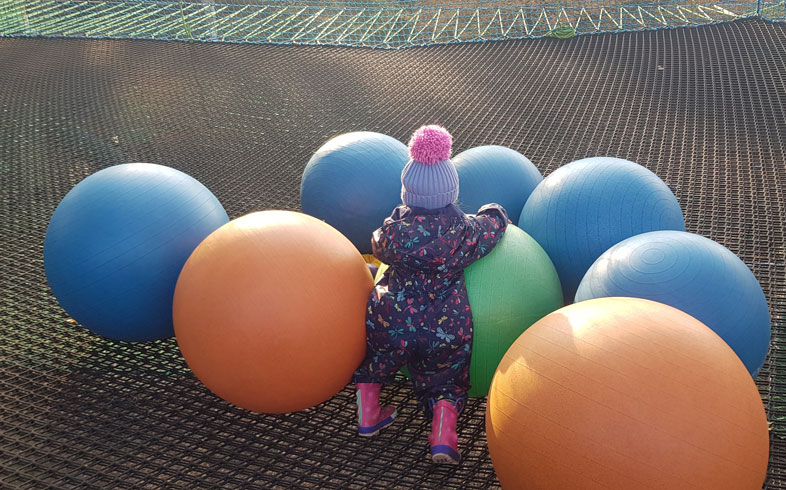 Toddler playing with over sized balls on a trampoline