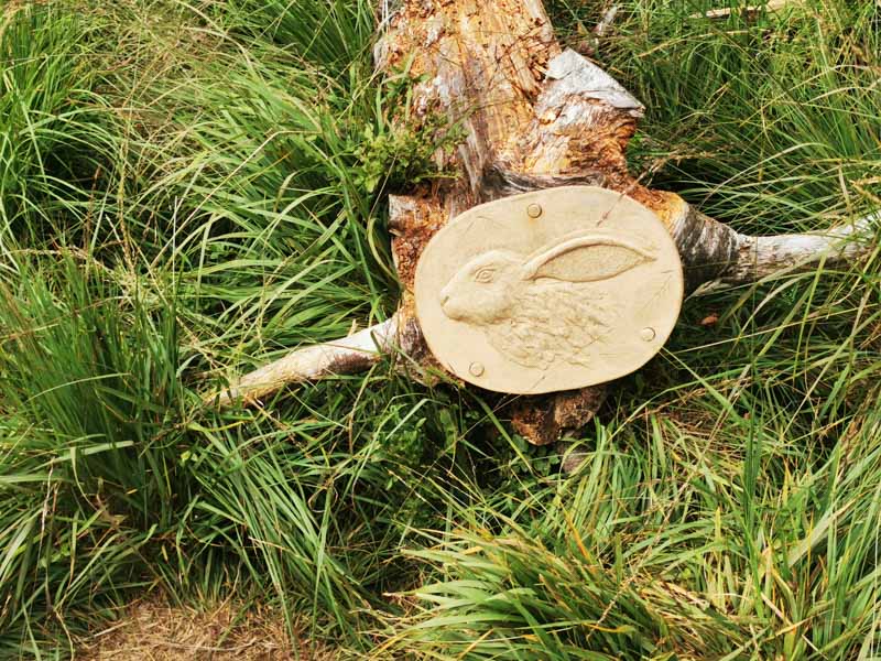 Ceramic plaque of a rabbit on a tree branch in the grass