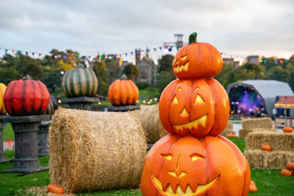Stack of decorative pumpkins with carved faces next to hay bales, outdoors