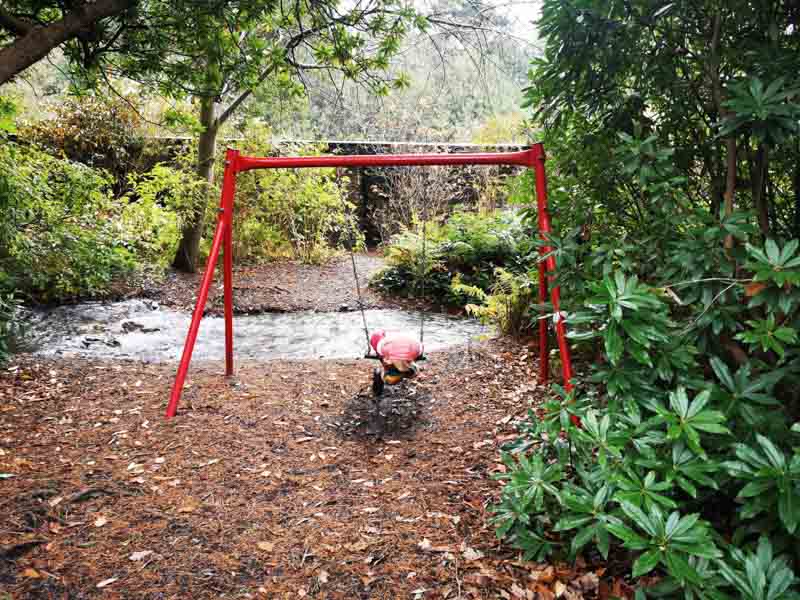 Red swing in woodland play area by stream