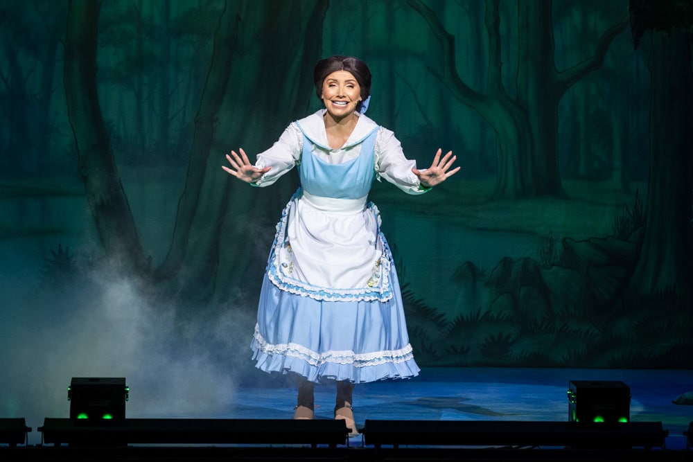 Belle on a stage with a fake forest behind her