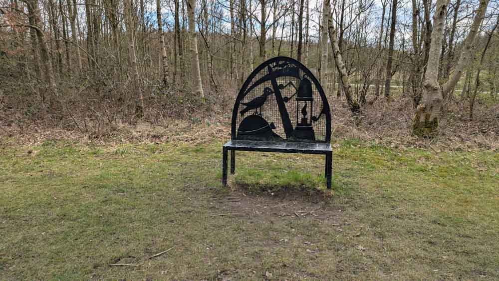 Black metal bench on grass with woods behind
