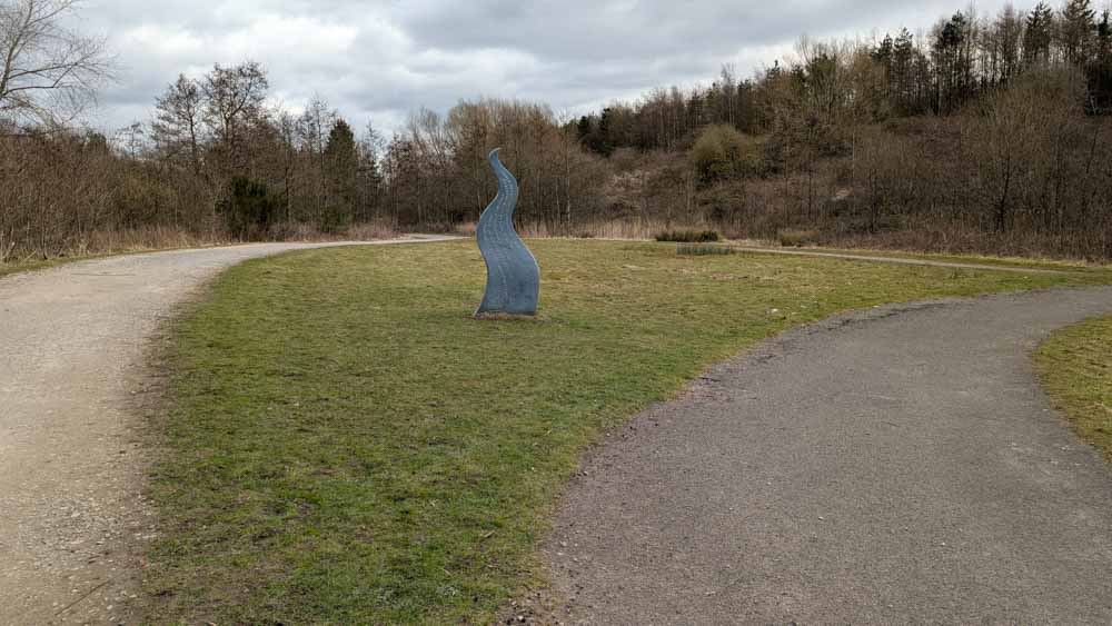Metal flame sculpture on grass with woodlands behind