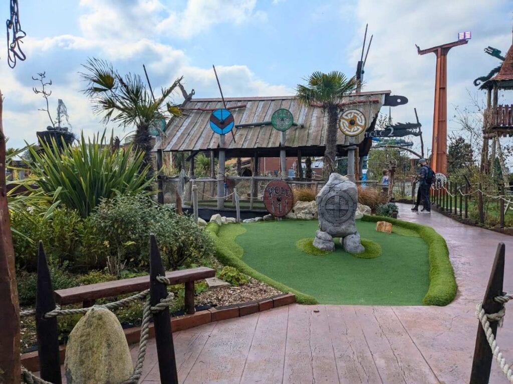 Crazy golf hole with wooden building behind looking like viking long house