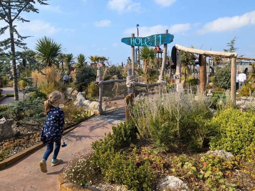 Small female child with gold club walking towards hole 11. Lots of beautiful planting