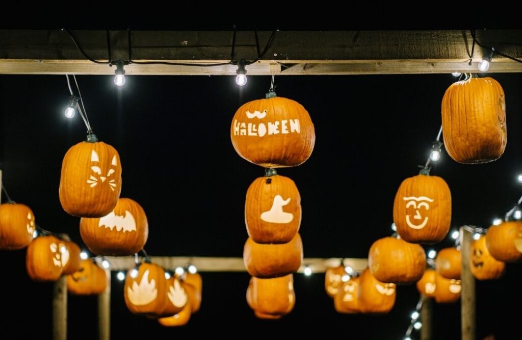 Carved pumpkins lit from within and strung up as lanterns at Walby Farm Park, glowing against the night sky with designs including faces, bats, and the word “Halloween.”
