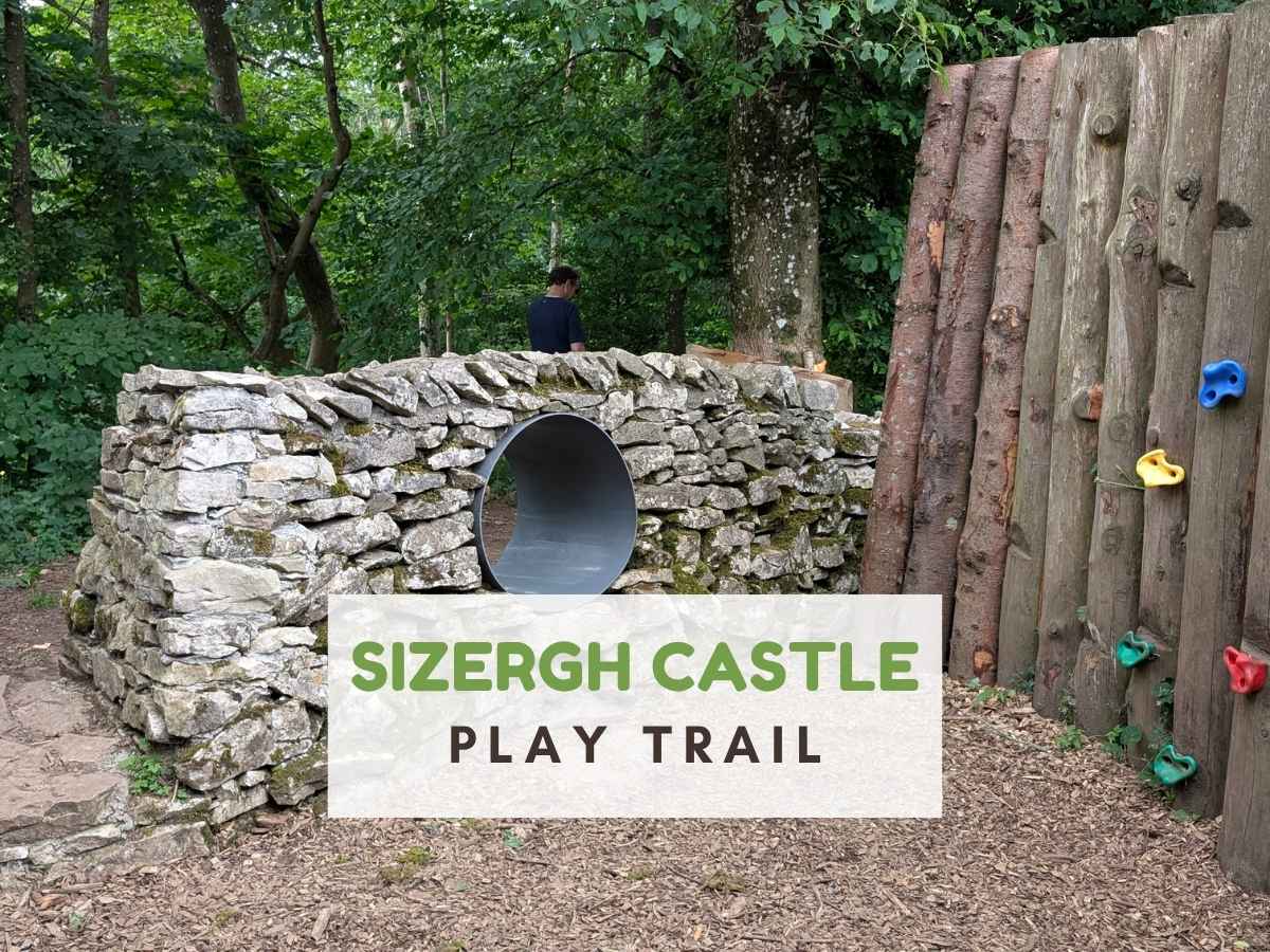 wooden climbing wall on one side and dry stone wall on the other with a grey plastic tunnel through it. Text reads Sizergh Castle Play Trail