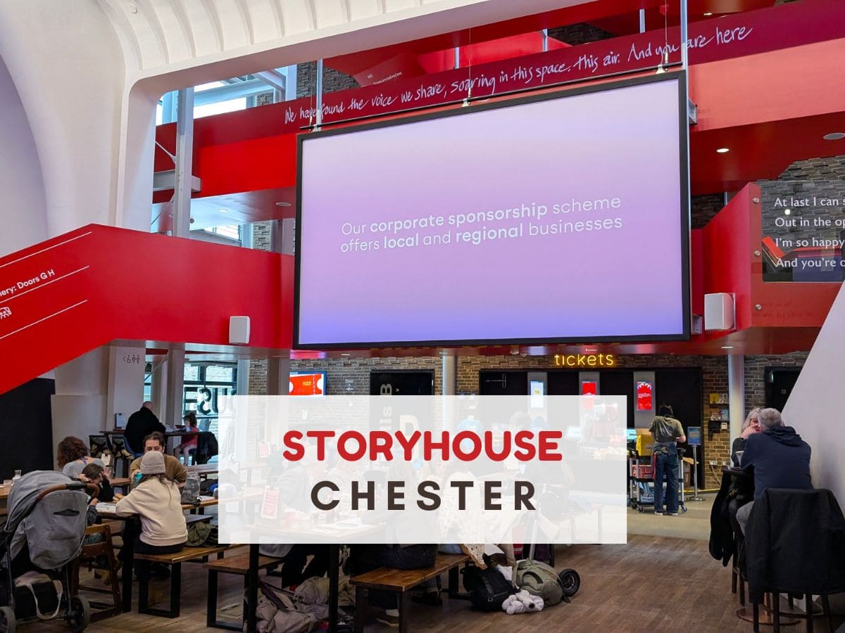 Inside a high ceiling red and white building with a large screen. Text reads Storyhouse Chester
